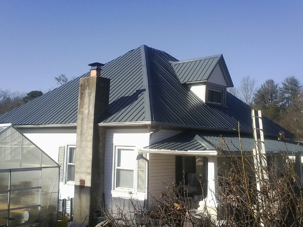 Dark blue standing seam metal roof on a white farmhouse with dormer — Slate & Tile Roof Repair by Roofing Brothers in Patchogue