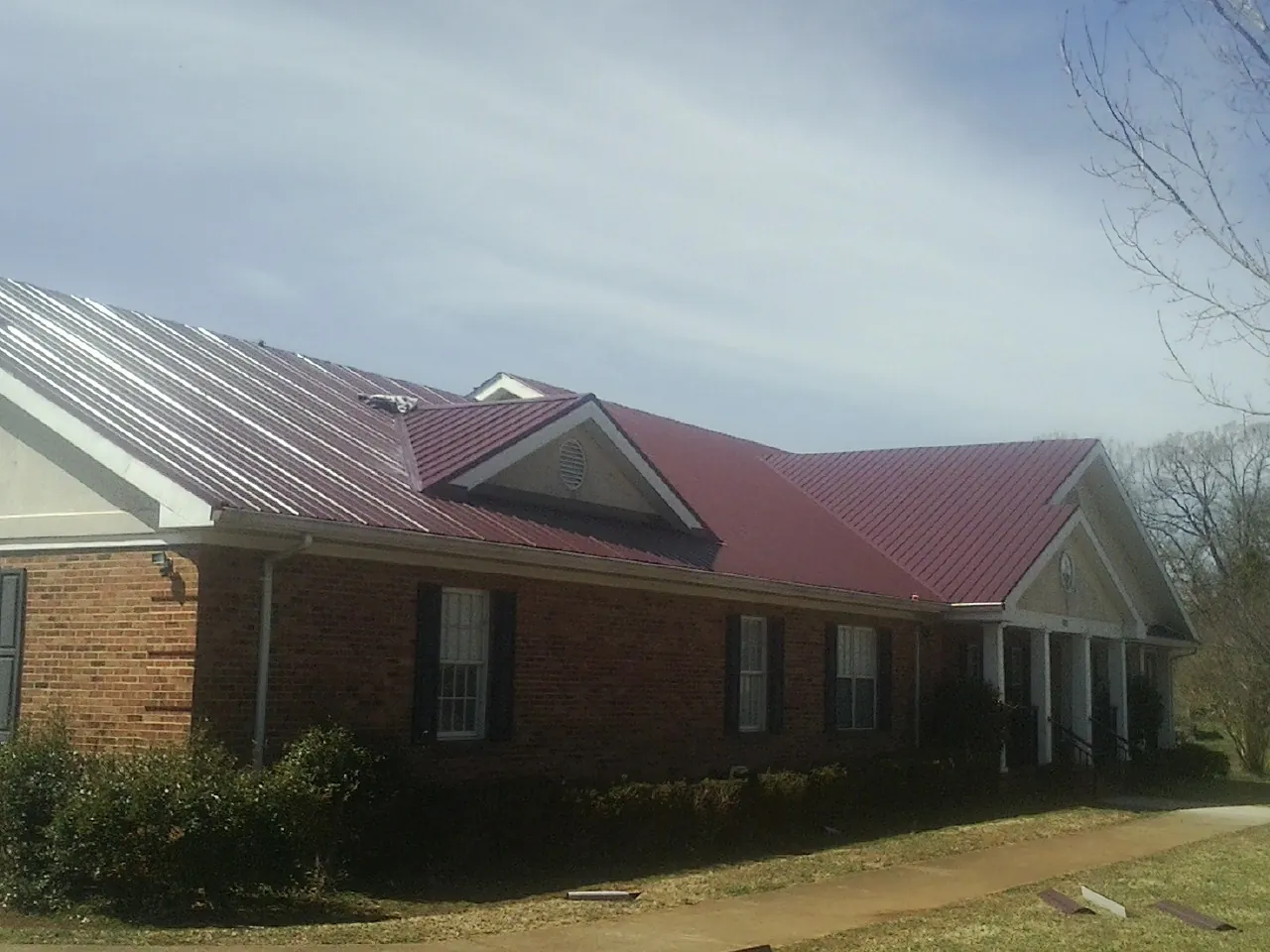 Red metal roof with gabled entries on a long brick building, from a Hail Damage Roof Repair job in Patchogue