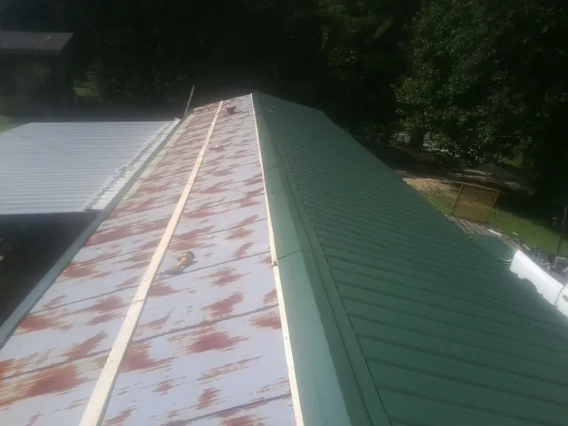Old rusted panels beside newly installed green metal roofing — Wind Damage Roof Repair by Roofing Brothers in Patchogue