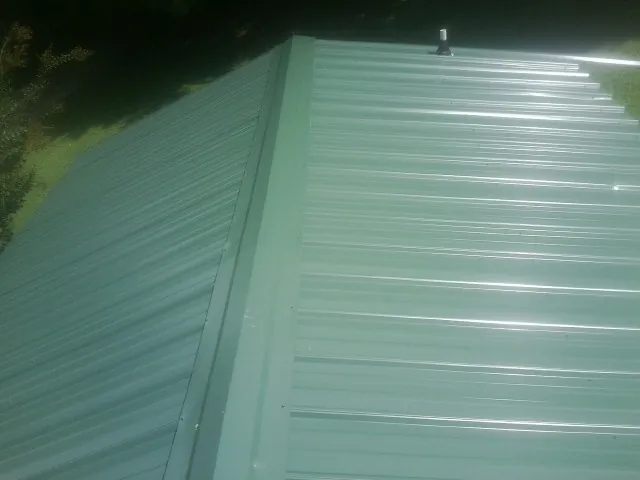 New green metal panels meeting at the ridge of a roof — Flat Roof Repair work by our crew in Patchogue